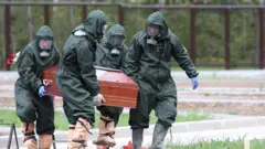 Люди в спецзащите с гробом