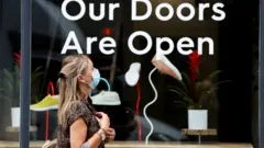 FILE PHOTO: A woman walks past a shop window near Covent Garden, wearing a protective mask under the new rules that enforce wearing face coverings in enclosed public spaces, amid the coronavirus disease (COVID-19) outbreak, in central London, Britain July 24, 2020