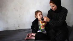 Shuruq trata de consolar a su hija Rafah, de 12 años, que como tantos otros niños sufre de desnutrición.