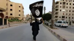 Miembro de Estado Islámico oncea una bandera de EI en Raqa, 29 de junio de 2014