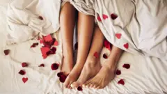 Les pieds d'un couple sortent du bas de la feuille entourés de cœurs en papier.