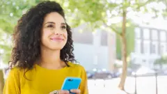 Une femme, téléphone en main, regarde vers l'horizon