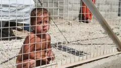 Child crouching behind a metal fence