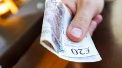A person holding a £20 note