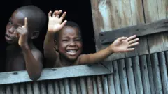 Des enfants font signe de la main par une fenêtre ouverte dans le bidonville de Makoko à Lagos