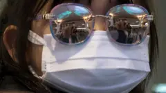 A girl wears a face mask and sunglasses
