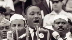 Martin Luther King standing in front of a crowd giving his "I have a dream" speech with numerous microphones in front of him