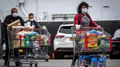 Consumidores americanos fora de um mercado com carrinhos cheios de compras