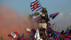 Vários manifestantes com bandeiras em cima de estátua em área externa no Chile