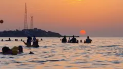 Les gens se baignent dans l'eau de la mer Méditerranée au large d'une plage de la capitale libyenne, Tripoli, près du coucher du soleil le 18 août 2020.