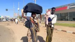 رجل وسيدة يحملان أمتعتهما في الشوارع فرارا من القتال الدائر