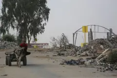 رجل فلسطيني يركب عربة يجرها حمار قرب حاجز خرساني (من الخلف) يُشير إلى "الخط الأصفر"