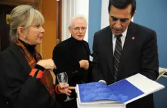Daphne y Chuck ven de negro en la presentación de su libro, que se ve abierto en primer plano. Ella sostiene una copa de vino vacía mientras habla con el congresista Darrell Issa.