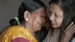 पीली साड़ी पहनी हुईं  सीरो देवी जो मोनिका को पकड़ कर रो रही हैं. 