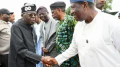 President Bola Tinubu wear all-black cloth dey shake hand SGF wey wear all-white cloth