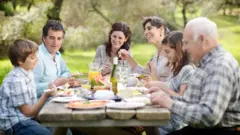 Piknik alanında tahta masa etrafında birlikte yemek yiyen bir aile