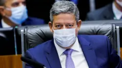 Arthur Lira olha em direção à câmera, sentado diante da mesa da Câmara