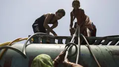 બાળકો પાણીના ટૅન્કર પર ચડ્યા છે.