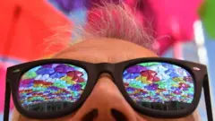 The reflection of colourful umbrellas in a person's sunglasses