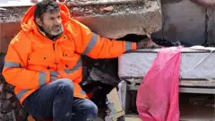 A man holds his dead daughter's hand as she is covered with debris.