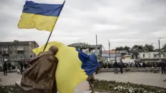 Ukrainian flag waves in front of statue in Kharkiv region
