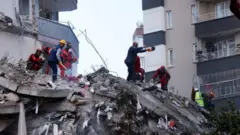 People and rescue workers stand on the rubble of a collapsed building following an earthquake in Adana, Turkey, February 7, 2023.