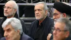 Mesud Pezeşkiyan, resmi yetkililer arasında şaşkın ve üzgün bir şekilde oturuyor. Bu bir anma toplantısı herkes siyah giyinmiş, bir kişi sarıklı.