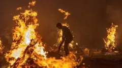 Workers and relatives stand around burning funeral pyres at night