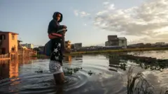 رجل يحمل طفلة ويعبر بها منطقة مغمورة بالمياه.