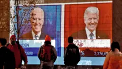 Trump / Biden on a screen with people watching on