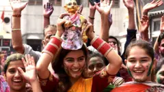 ਅੰਮ੍ਰਿਤਸਰ ਦੇ ਦੁਰਗਿਆਣਾ ਮੰਦਿਰ ਵਿੱਚ ਹੋਲੀ ਦੌਰਾਨ ਸਿਰ 'ਤੇ ਲੱਡੂ ਗੋਪਾਲ ਦੀ ਮੂਰਤੀ ਚੁੱਕੀ ਭੀੜ ਵਿੱਚ ਜਾ ਰਹੀਆਂ ਕੁੜੀਆਂ ਖੁਸ਼ੀ ਦੇ ਰੌਂਅ ਵਿੱਚ, 18 ਮਾਰਚ, 2022