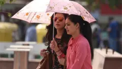 వేసవి నుంచి రక్షణకు గొడుగులో వెళ్తున్నవారు