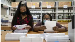 Working in bipartisan pairs, canvassers process mail-in ballots in Maryland, the earliest state to process postal votes in the country