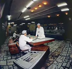 Imagem colorida de arquivo mostrando dois trabalhadores de macacão e chapéu brancos em uma mesa de controle da usina nuclear de Chernobyl, em abril de 1983.