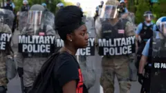 Black woman in front of police in riot gear