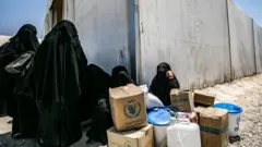 Perempuan di kamp Al-Hol, duduk di dekat kotak-kotak bantuan.