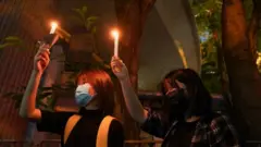 Dos mujeres levantan velas en el parque Victoria de Hong Kong.