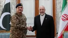 O presidente do Parlamento iraniano, vestindo um paletim escuro sobre uma camisa branca, aperta a mão do chefe do Exército do Paquistão, que usa uniforme militar e um boné verde.