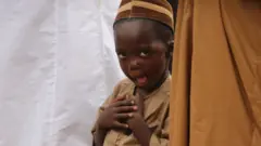 A young boy makes a funny face at the camera during prayers.