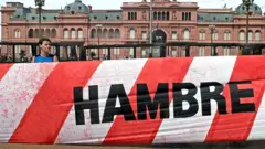 Un joven con un cartel que se lee "hambre" con la Casa Rosada de fondo.
