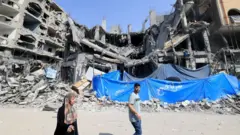 Palestinians walk past a building damaged in an Israeli air strike in Khan Younis
