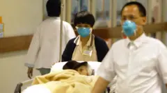 হংকং ২০০৩, একজন সার্স রোগীকে নিয়ে যাচ্ছেন স্বাস্থ্যকর্মীরা