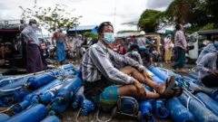A man sits on empty oxygen canisters in Manalay