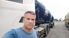 Retrato de Wanderlei Dedeco, um homem branco de meia idade de cabelos grisalhos, com caminhão branco e preto ao fundo
