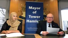 বিশিষ্ট বাঙালি ব্যক্তিত্বদের নামে ভবনের নামকরণ প্রসঙ্গে সংবাদ সম্মেলনে বক্তব্য রাখছেন টাওয়ার হ্যামলেটস কাউন্সিলের নির্বাহী মেয়র জন বিগস। পাশে উপ-মেয়র আসমা বেগম।