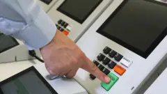Dedo apertando tecla CONFIRMA da urna