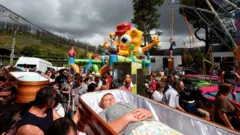 Pessoas levam nos ombros um caixão, em frente a um brinquedo do personagem Bob Esponja