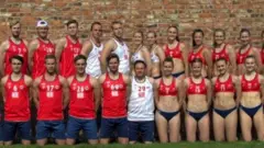 The male and female Norwegian teams pose side by side, the men wearing shorts and long tank tops, the women wearing small bikini tops and bottoms.