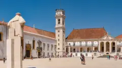 Torre da Universidadejoguinho das frutasCoimbra diantejoguinho das frutaspátio com pessoas caminhandojoguinho das frutasum diajoguinho das frutassol; há uma estátuajoguinho das frutascostas