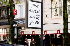Um outdoor com a frase “My Heart Will Go On” aparece tendo ao fundo uma brasserie parisiense